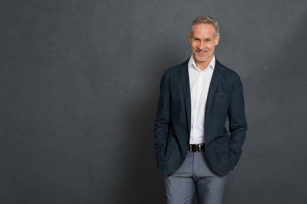 Happy senior businessman Happy senior businessman wearing suit standing over grey wall and looking at camera. Portrait of successful leader standing isolated gray background with copy space. Handsome mature man with fashion clothes. hands in pockets stock pictures, royalty-free photos & images