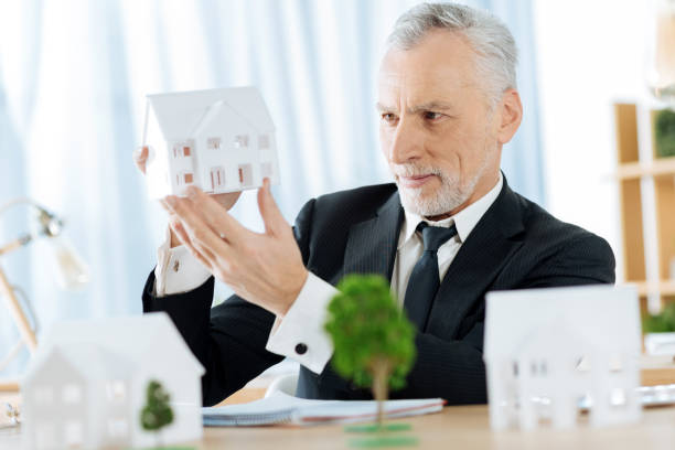 istock Smiling real estate agent holding a miniature of a house while working 901093742