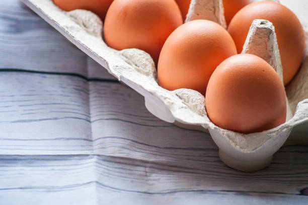 istock Close-up view of raw chicken eggs in egg box on white wooden background 901097252