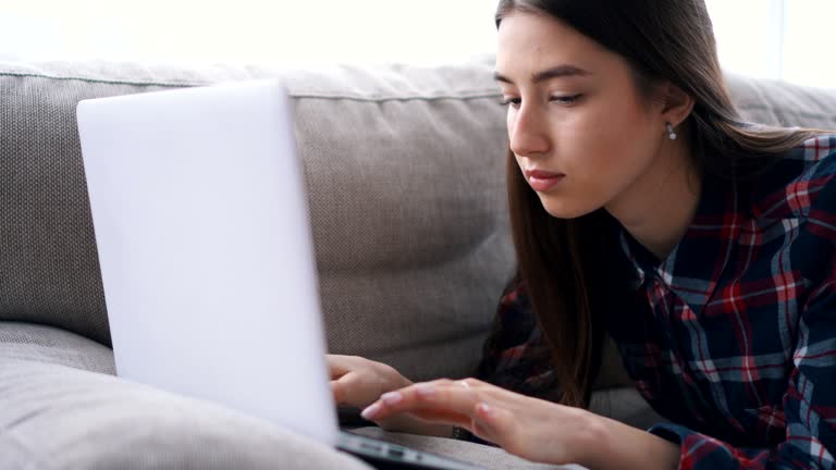 Girl typing on keyboard of laptop on sofa