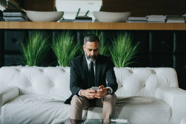 istock Middle-aged businessman using mobile phone in modern office on sofa 901138188