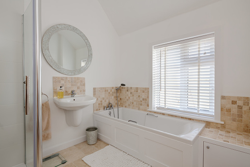Bright white home restroom with wall handwash basin compact bath and shower, large circular mirror venetian window blind and tiled splashback