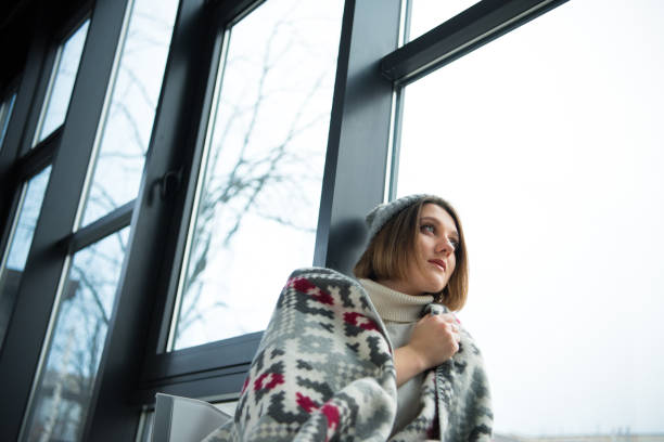 Beautiful girl wrapped in warm blanket looking at the window