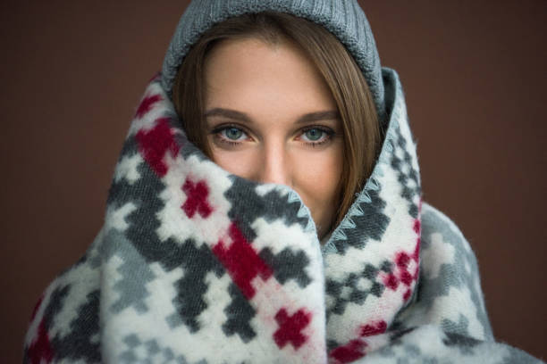 Portrait of woman wrapped in blanket and wearing gray hat isolated on brown