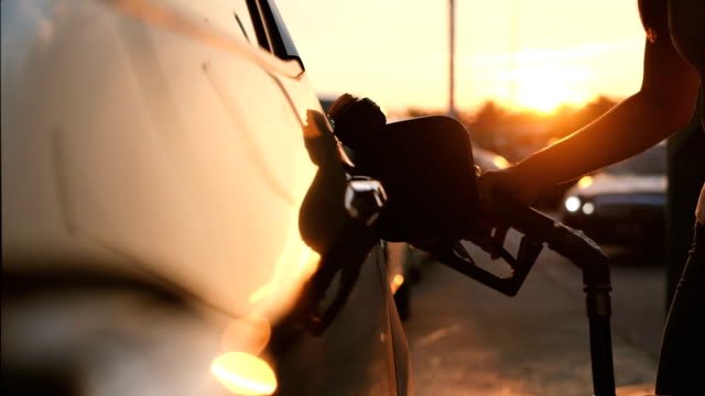 Woman refueling car at gas station pump at sunset