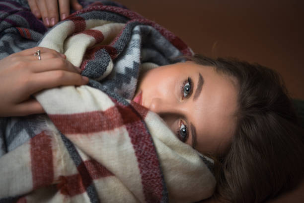 Woman lying on a floor wrapped in blanket and looking at camera isolated on brown