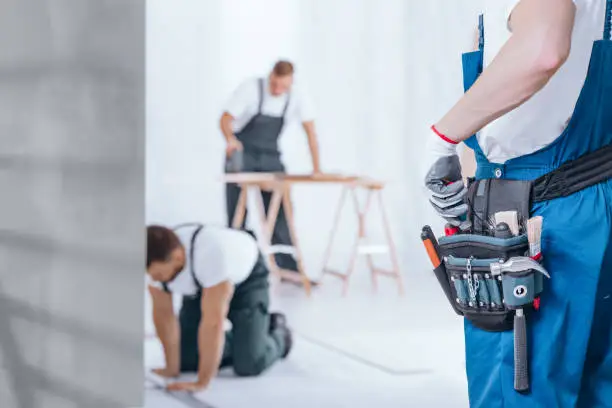Close-up of handyman with glove on hand and tool belt on blue trousers during home renovation