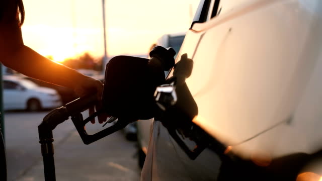 Woman refueling car at gas station pump at sunset with flare