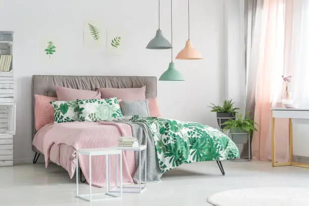 Pastel beddings on stylish bed in white bedroom with plants