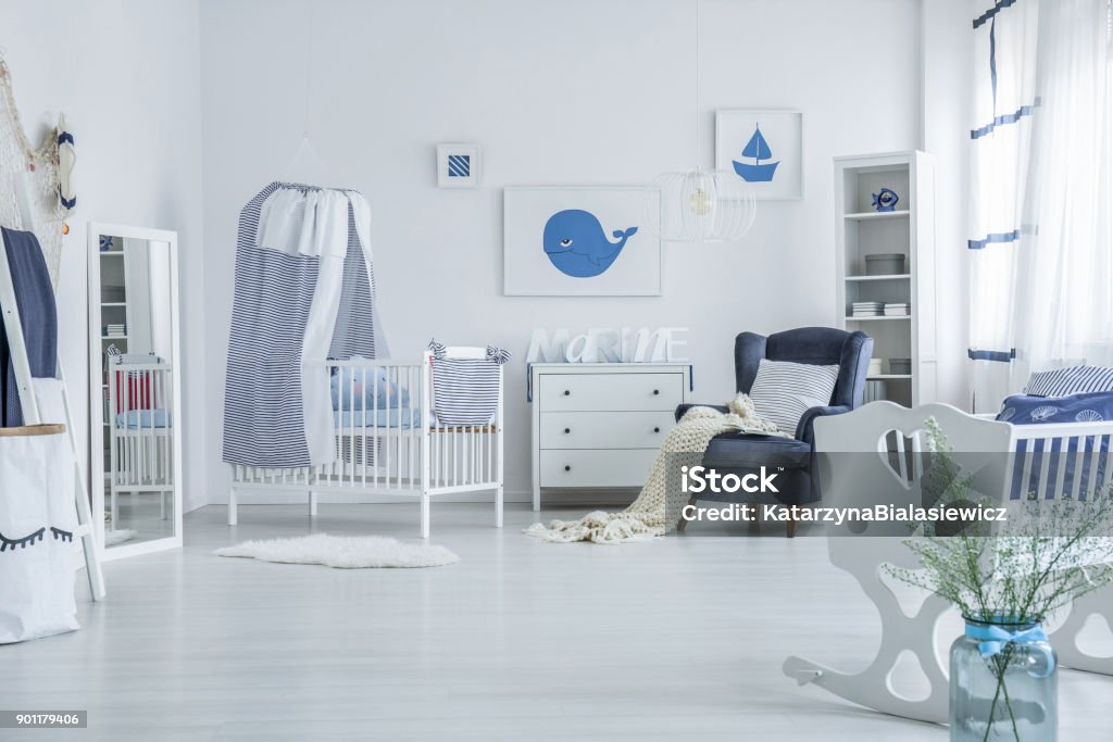 Spacious baby's room with crib Vase next to white cradle in spacious baby's room with blanket on armchair and striped veil above crib Domestic Room Stock Photo