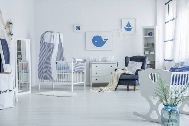 Spacious baby's room with crib Vase next to white cradle in spacious baby's room with blanket on armchair and striped veil above crib nursery bedroom stock pictures, royalty-free photos & images