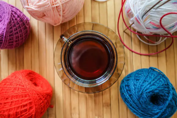 Knitting wool and black tea as a concept of coziness and a home hobby. A mug of fragrant drink in the center. Clusters of knitting thread on the table.