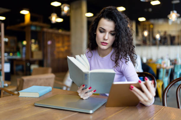 istock Young woman reading book and holding tablet 901195254