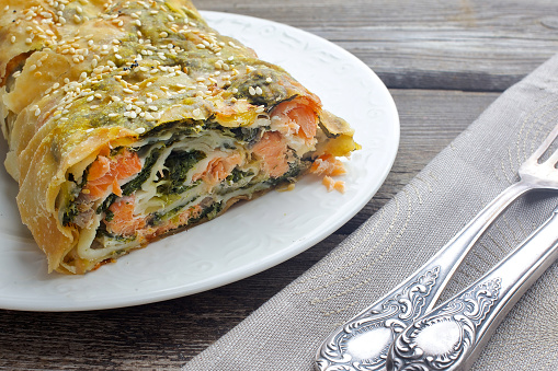 Strudel pie with salmon and spinach, served on wood background
