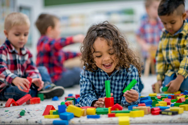 Playtime For Kids A group of preschool kids are playing indoors at a daycare center. One boy is lying on the floor and playing with colorful toy blocks. toddlers playing stock pictures, royalty-free photos & images