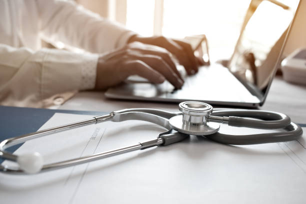istock Doctor's working on laptop computer, writing prescription clipboard with record information paper folders on desk in hospital or clinic, Healthcare and medical concept. Focus on stethoscope 901209162