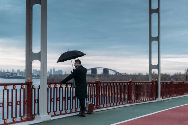 istock stylish lonely man with umbrella and suitcase standing on bridge 901215890