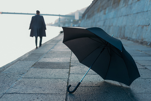 umbrella lying on river shore while man walking blurred on background