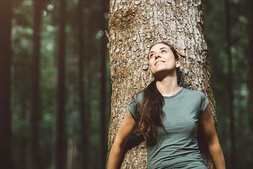 Woman smiling and relaxing in nature, she is leaning on a tree and looking away