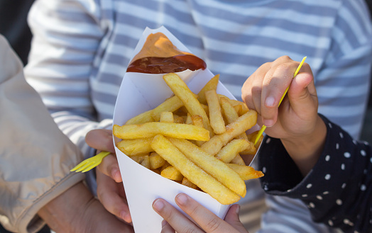 French fries with ketchup and curry sauce in the white box on woman and kid hands