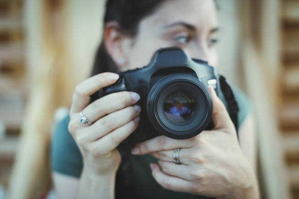 Pensive woman looking away and holding a professional digital camera, she is sitting outdoors