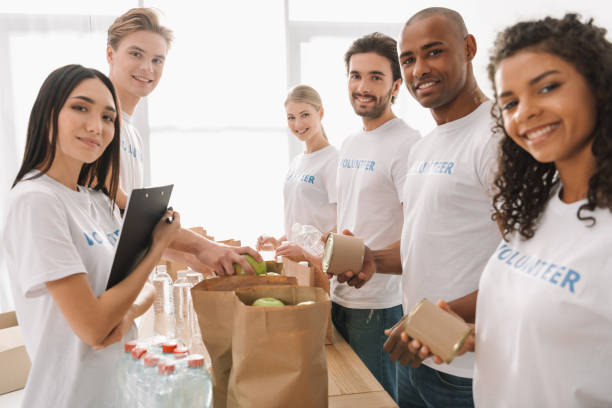 multiethnic group of volunteers multiethnic group of volunteers putting food and drinks in paper bags and looking at camera the black womens expo stock pictures, royalty-free photos & images