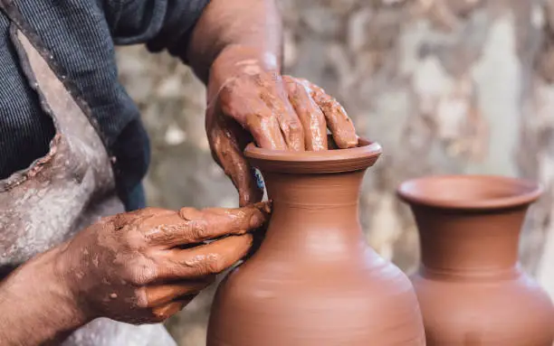 Close up view of an adult male using their own hands to make a ceramic vase.