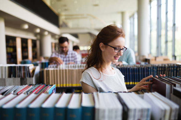 ritratto di una ragazza piuttosto sorridente che legge libro in biblioteca - book library bookshelf university foto e immagini stock