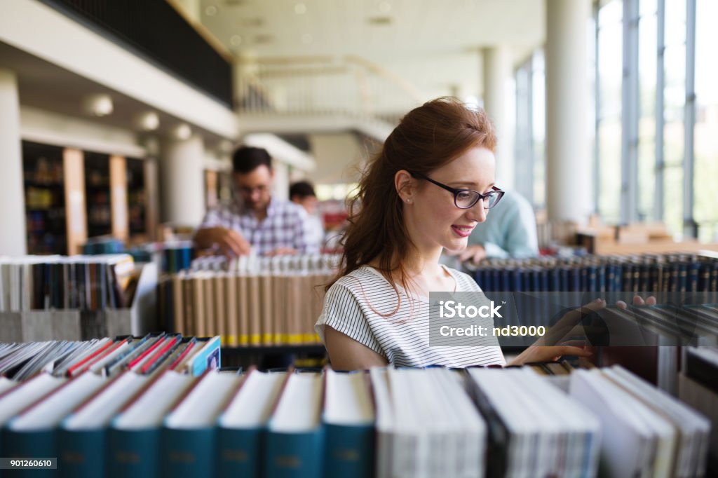 Portrait of a pretty smiling girl reading book in library Portrait of a pretty smiling girl reading book indoors in library Library Stock Photo