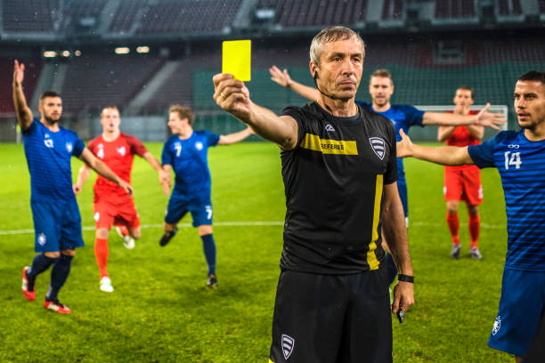 Soccer referee showing yellow card Soccer referee surrounded by players of both teams while he is holding a yellow card. referee stock pictures, royalty-free photos & images