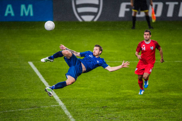 Soccer player performing a volley shot Soccer player in a blue jersey in mid-air in the penalty area about to perform a volley shot. soccer soccer ball kicking adult stock pictures, royalty-free photos & images