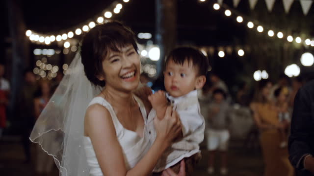 Happy woman holding and playing with her son at wedding party.