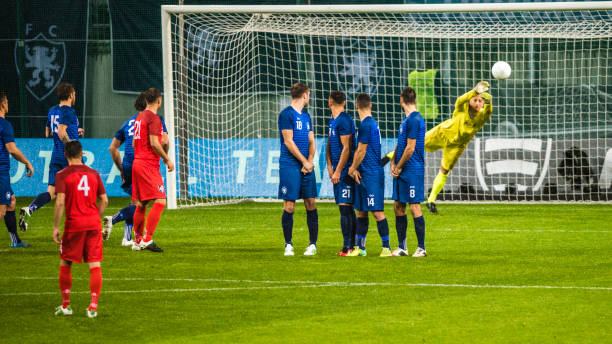 Free kick Soccer goalkeeper in yellow preparing to defend the goal from the ball that is flying over the human defensive wall. defending sport stock pictures, royalty-free photos & images