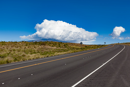 road to beautiful mauna kea volcano under huge cloud on big island, hawaii islands.