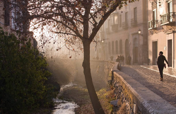 GRANADA, ANDALUCIA, SPAIN - DECEMBER 20, 2017: Woman walks by Carrera del Darro river in afternoon sunhaze on December 20, 2017 in Granada, Andalucia, Spain
