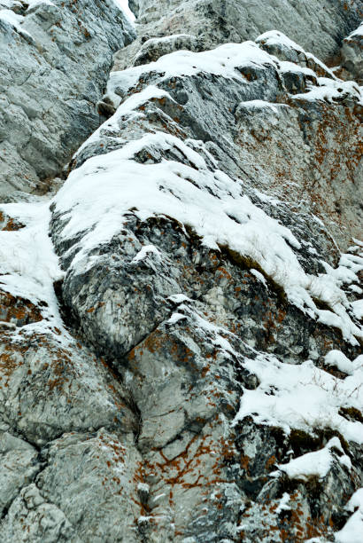 vertical background: a fragment of the wall of a natural cliff with snow-covered ledges\