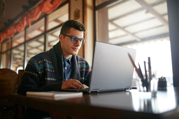 Handsome freelancer businessman working on laptop in cafe. Blogger man updating his profile in social networks with photos sharing with followers multimedia using notebook with wifi. Nerd in glasses Handsome freelancer businessman working on laptop in cafe. Blogger updating his profile in social networks with photos sharing with followers multimedia using notebook with wifi. nerd sweater stock pictures, royalty-free photos & images