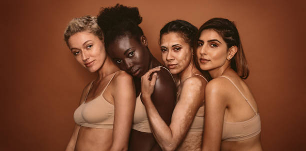 Multi ethnic female friends standing together Group of beautiful young women standing together on brown background. Multi ethnic female friends in studio looking at camera. black skin stock pictures, royalty-free photos & images