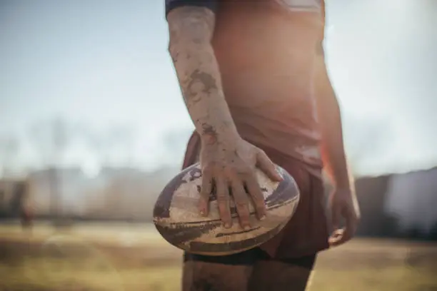 One man, rugby player covered in mud, holding rugby ball in his nads, part of.