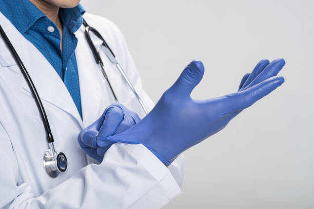 Male hands wearing blue gloves Saving life. Close up of tender male arms pulling on one time gloves  while shoot on the isolated background surgical glove stock pictures, royalty-free photos & images