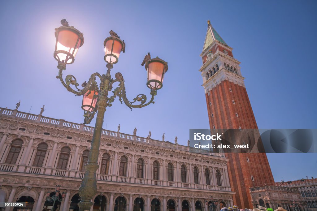 View from Piazza San Marco. View from Piazza San Marco of the Campanile Bell Tower in St Marks Sq. With ornate street lamps in the foreground blocking the glare of the summer sun. In Venice, Italy. Architecture Stock Photo