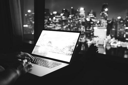Woman freelancer is working using laptop computer in home office at night. Aerial city skyline view from window. Freelance lifestyle