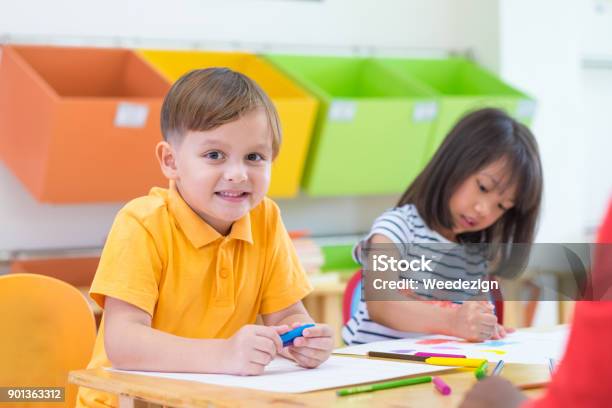 Caucasian Boy Ethnicity Kid Smiling White Learning In Classroom With Friends And Teacher In Kindergarten School Education Concept Stock Photo - Download Image Now