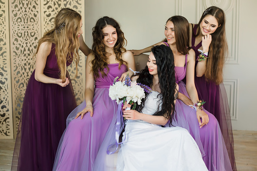 La tala entusiasmado con la boda. Atractivo joven novia con un ramo de novia y sonriendo mientras hablaba con sus encantadoras damas de honor en vestidos de púrpura photo