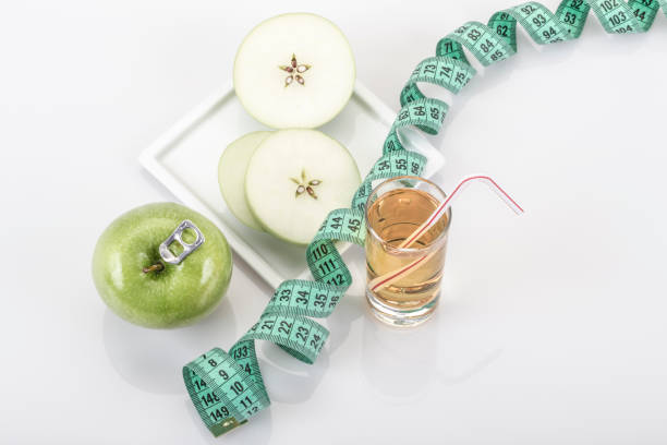 A green apple fruit and juice surrounded with green measurement tape on white with reflection