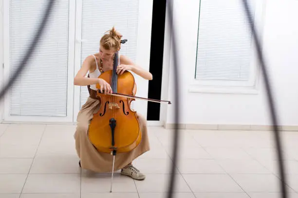 Young woman playing violoncello at home.