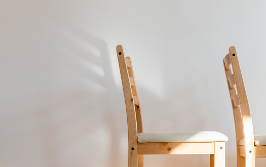 Chair dreaming of wings; two wooden chairs before a clean white wall, the back of one of casts a wing-shaped shadow