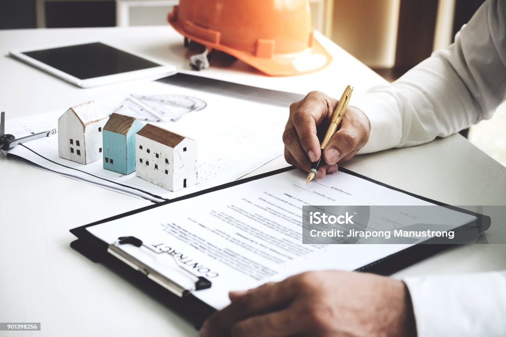 Businessmen are checking the contract to use the right pen. Signed building approval with blueprint and house model on the table. Real Estate Stock Photo