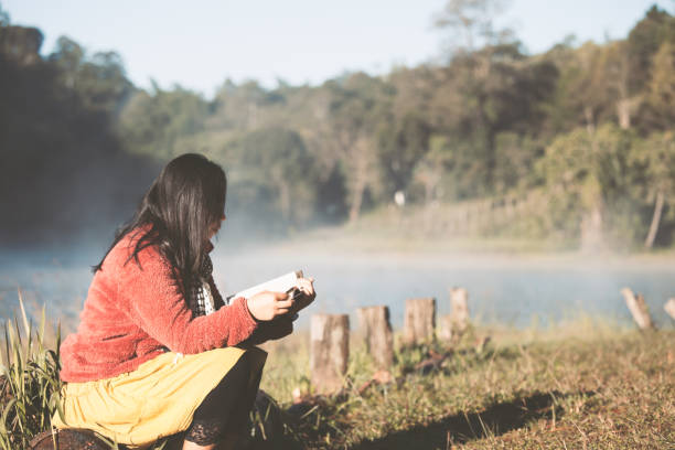 joven mujer leyendo un libro en el parque natural con la frescura de la mañana con la luz del sol - lake asia young women beautiful people fotografías e imágenes de stock