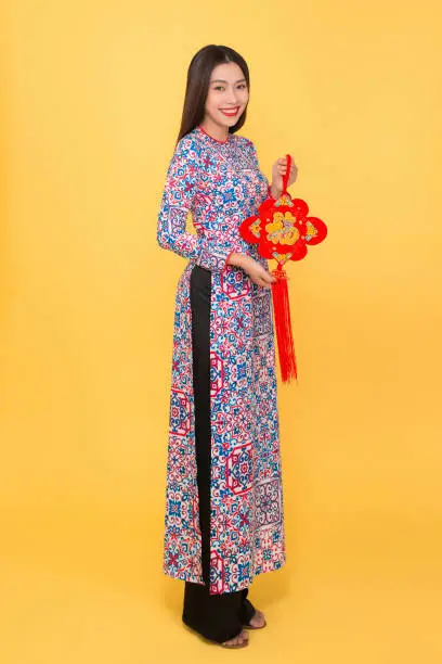 Full-length portrait of Vietnamese girl in ao-dai dress holding attributes. Text mean Happiness